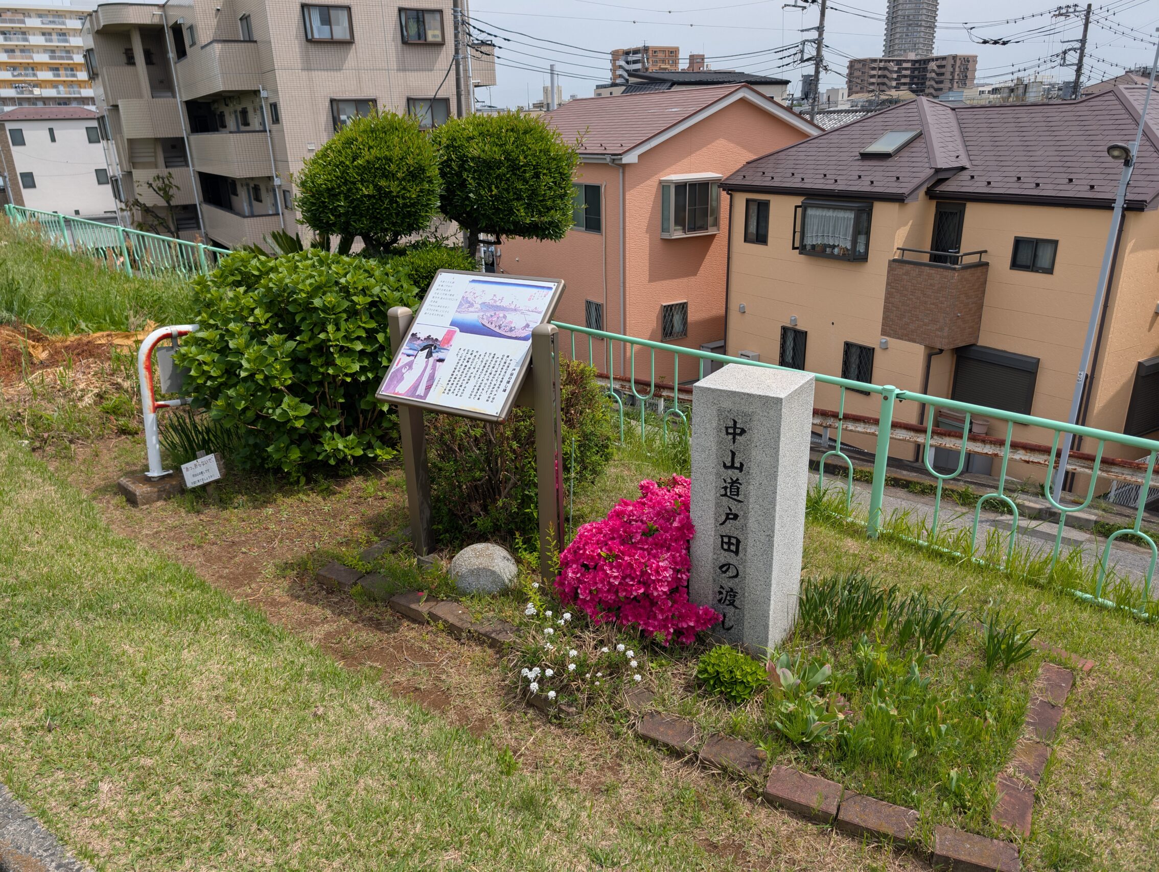 A stone marker and information sign on a steep grassy slope, with flower beds.
