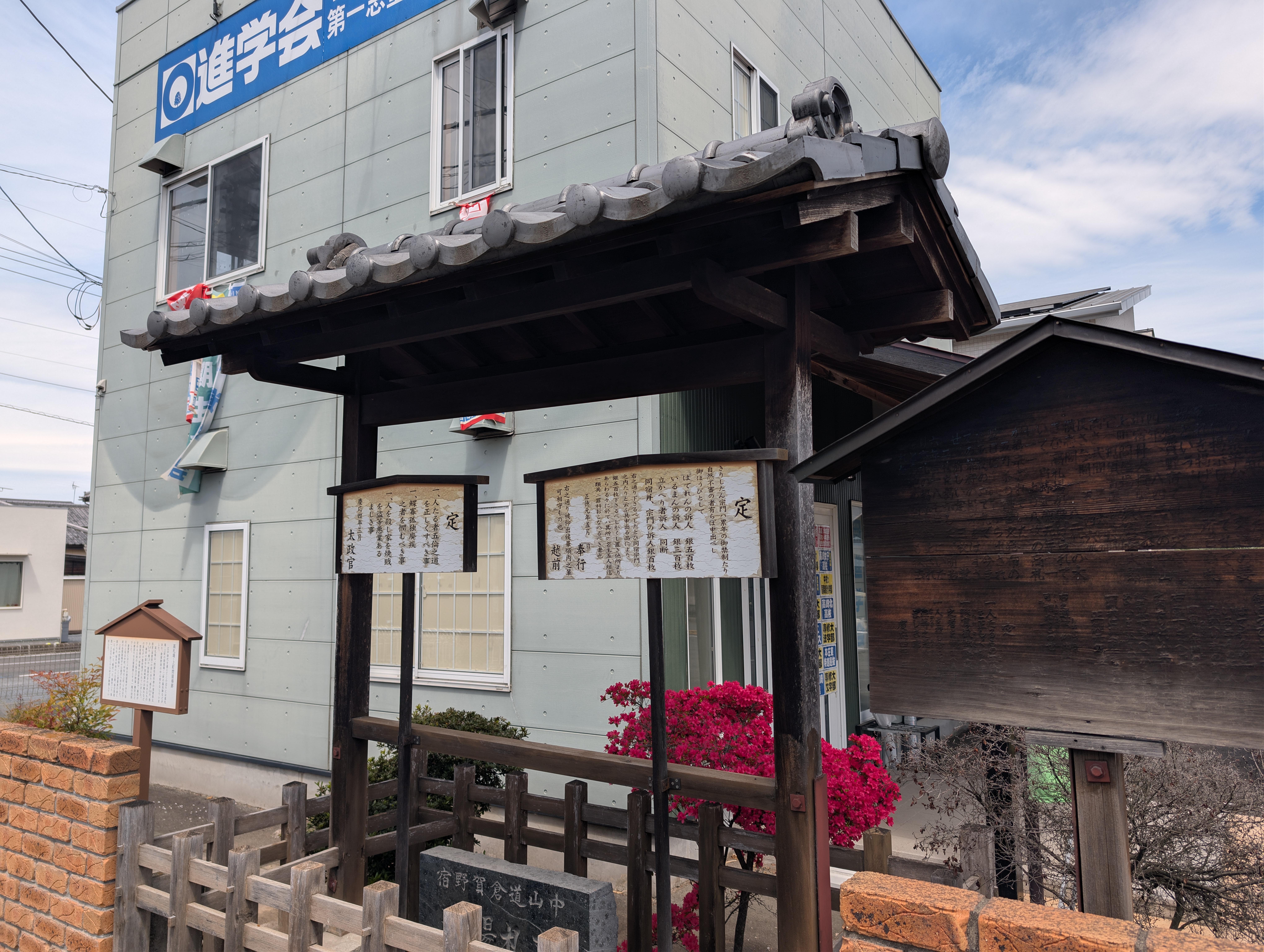 A wooden structure that functions as a message board with a couple of signs hanging from the roof.