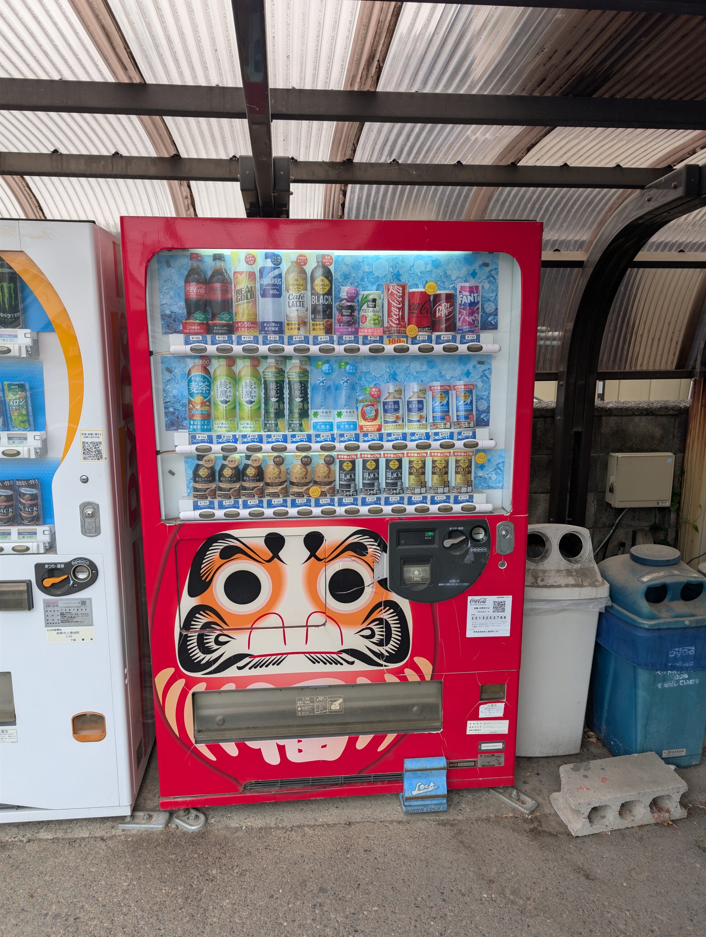 A red vending machine with a large picture of a darumi doll gracing the outside of the box.