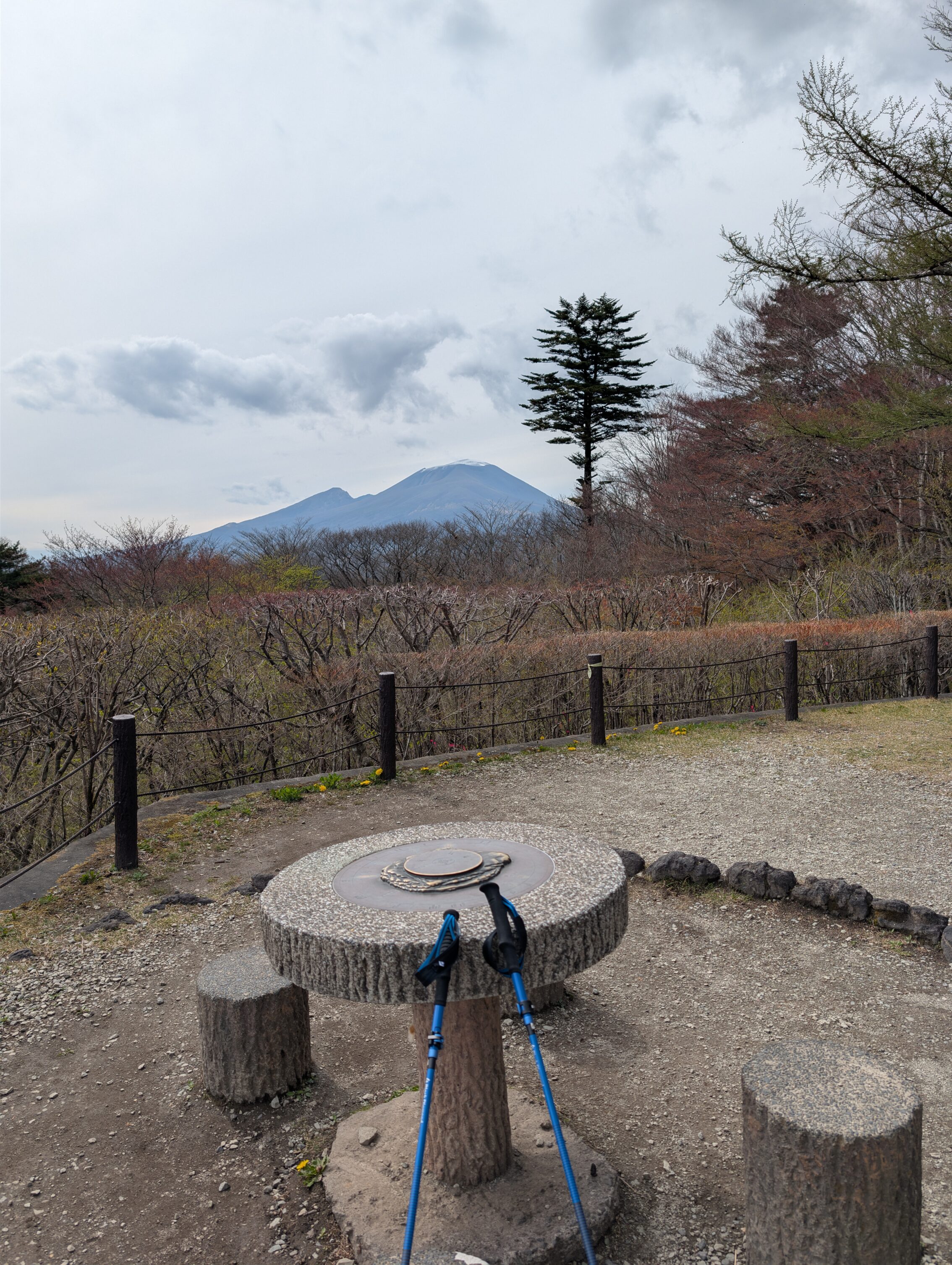 A compass rose on a stone table, with two hiking poles leaning on it. Mount Asama and a smaller peak is showing in the distance.