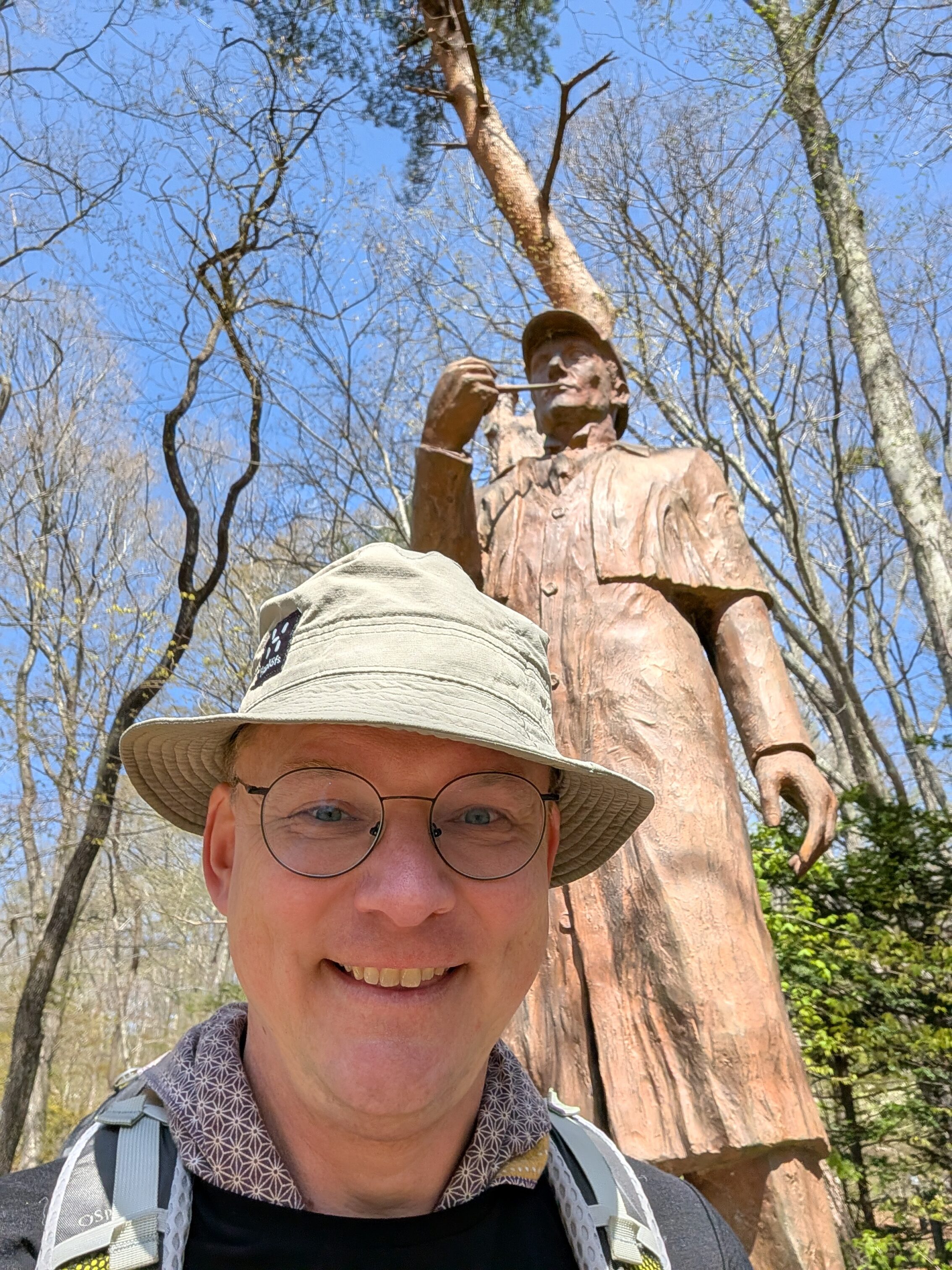 A living person with a hat in front of a statue of Sherlock Holmes.