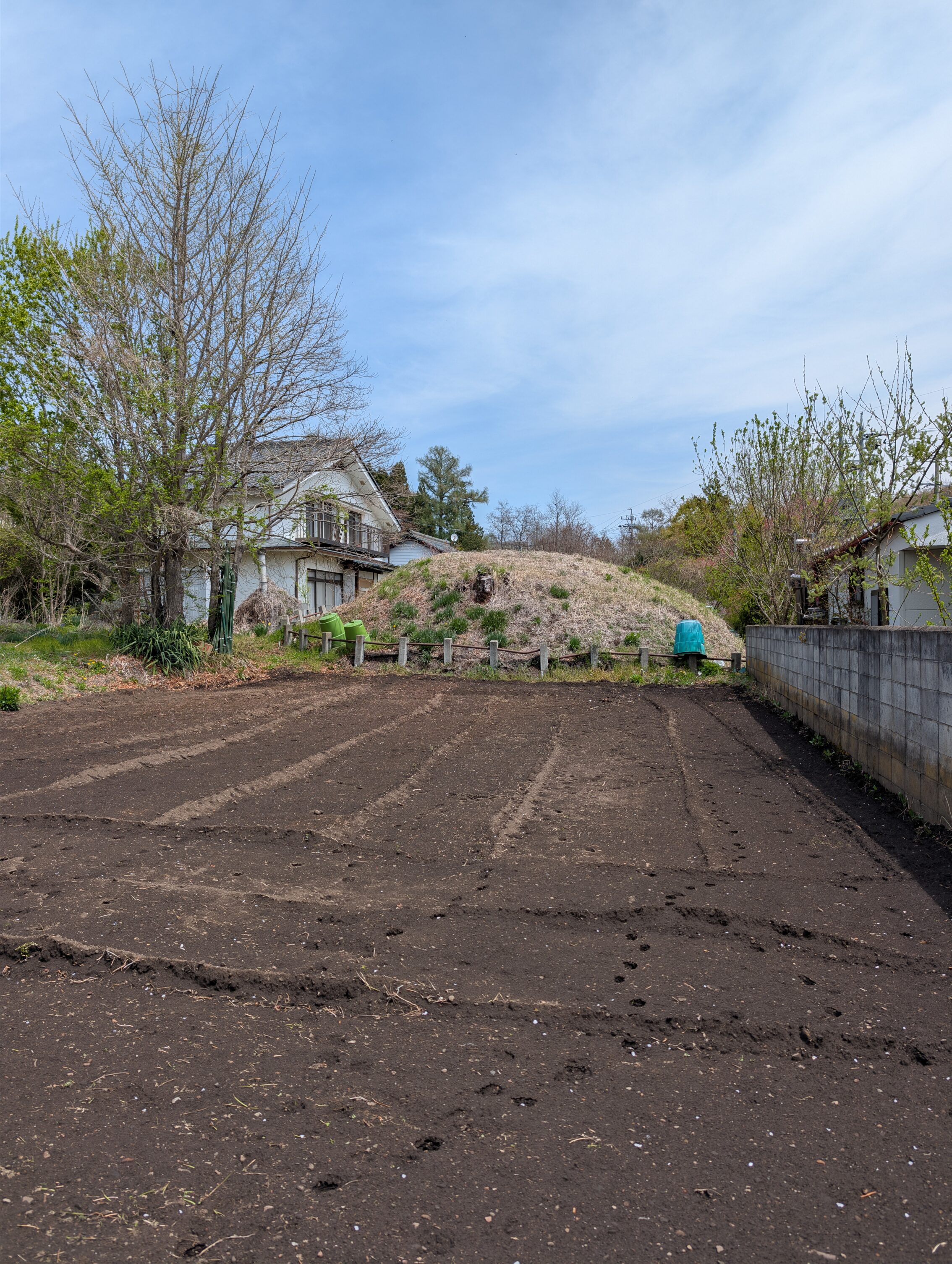 A small mound behind some houses and a small tilled field.