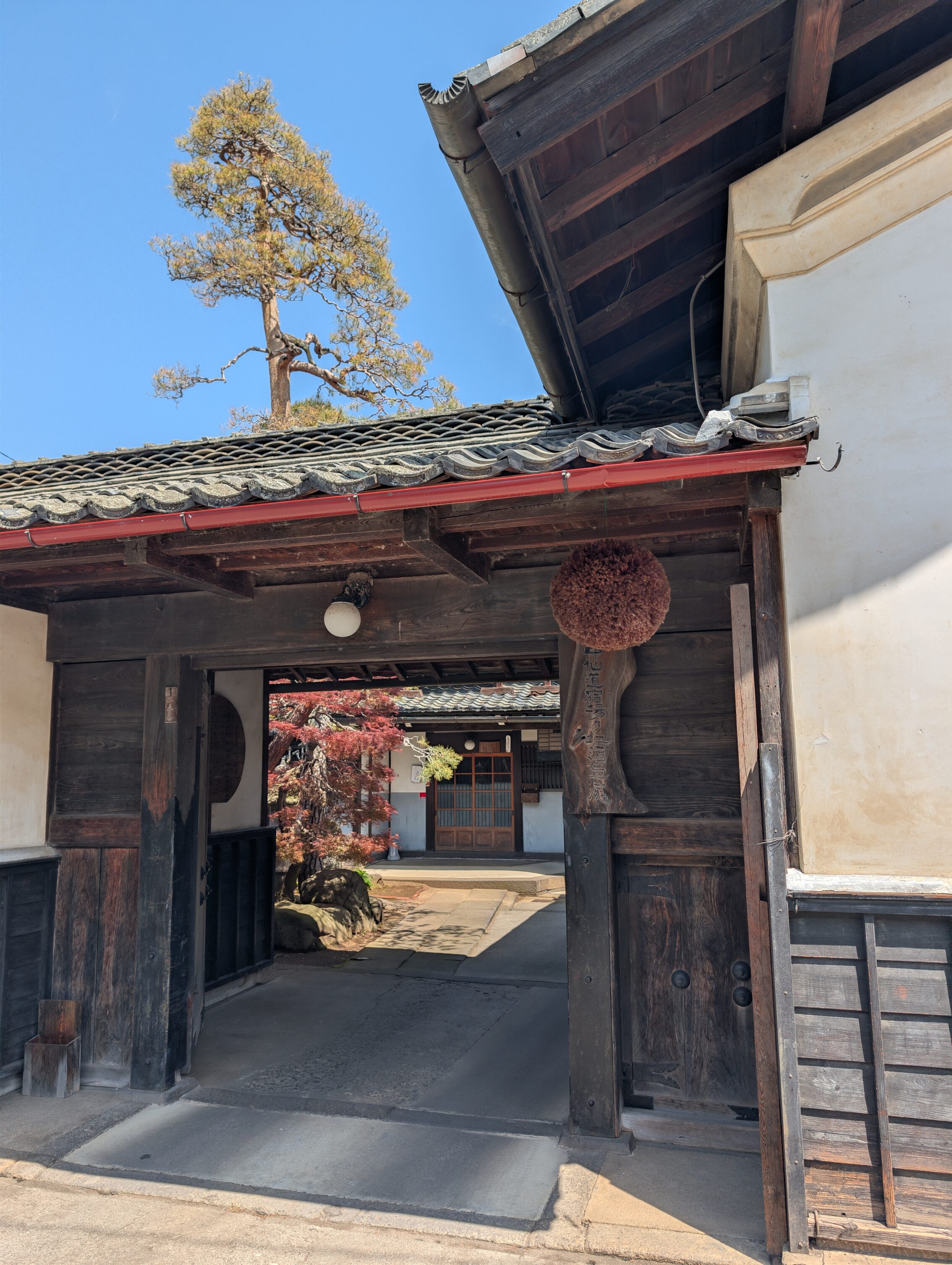 A open gate to a an old house with a sugidama ball hanging on the right hand side.