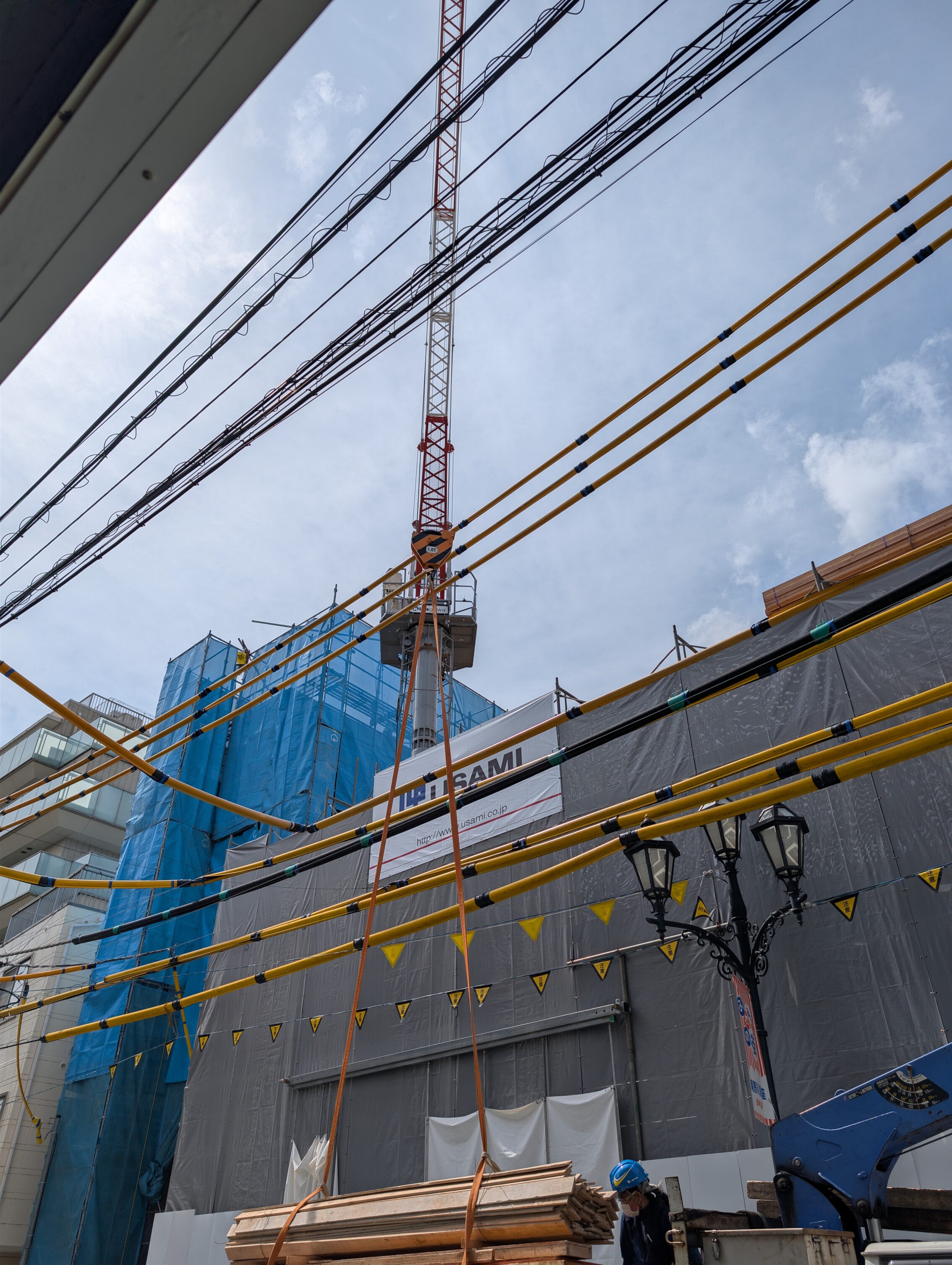 Overhead electrical cables amongst city houses, with a crane lifting stuff up inbetween them.