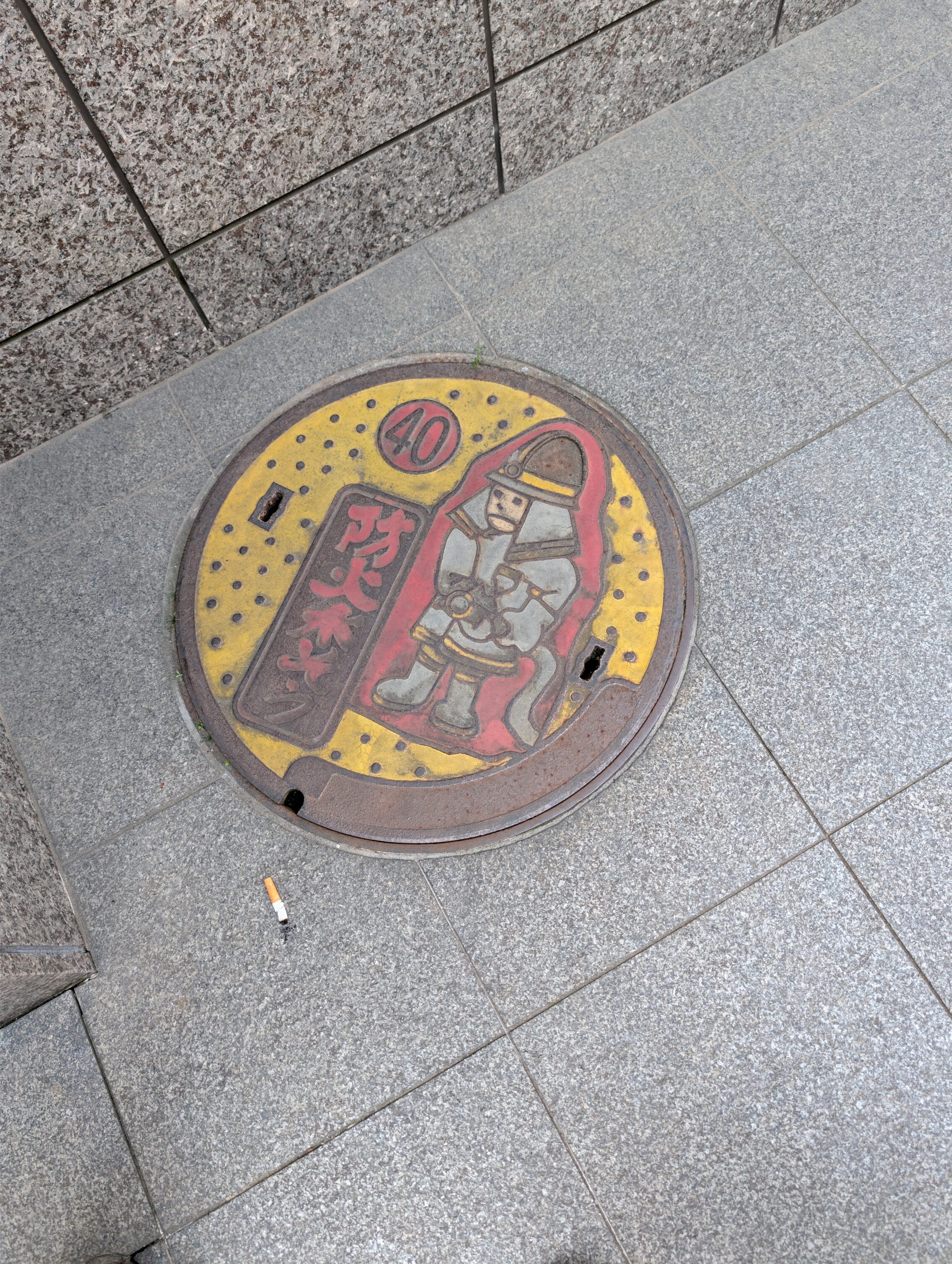 A manhole cover with a firefighter on it, in colour.