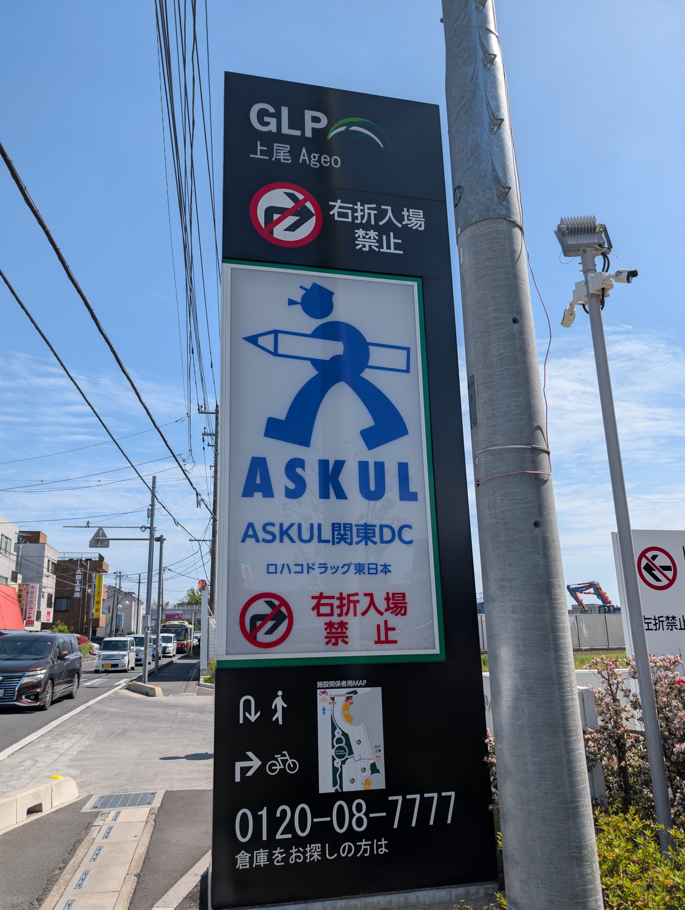 A sign by a road showing a stick figure carrying a huge crayon, and the text "ASKUL".