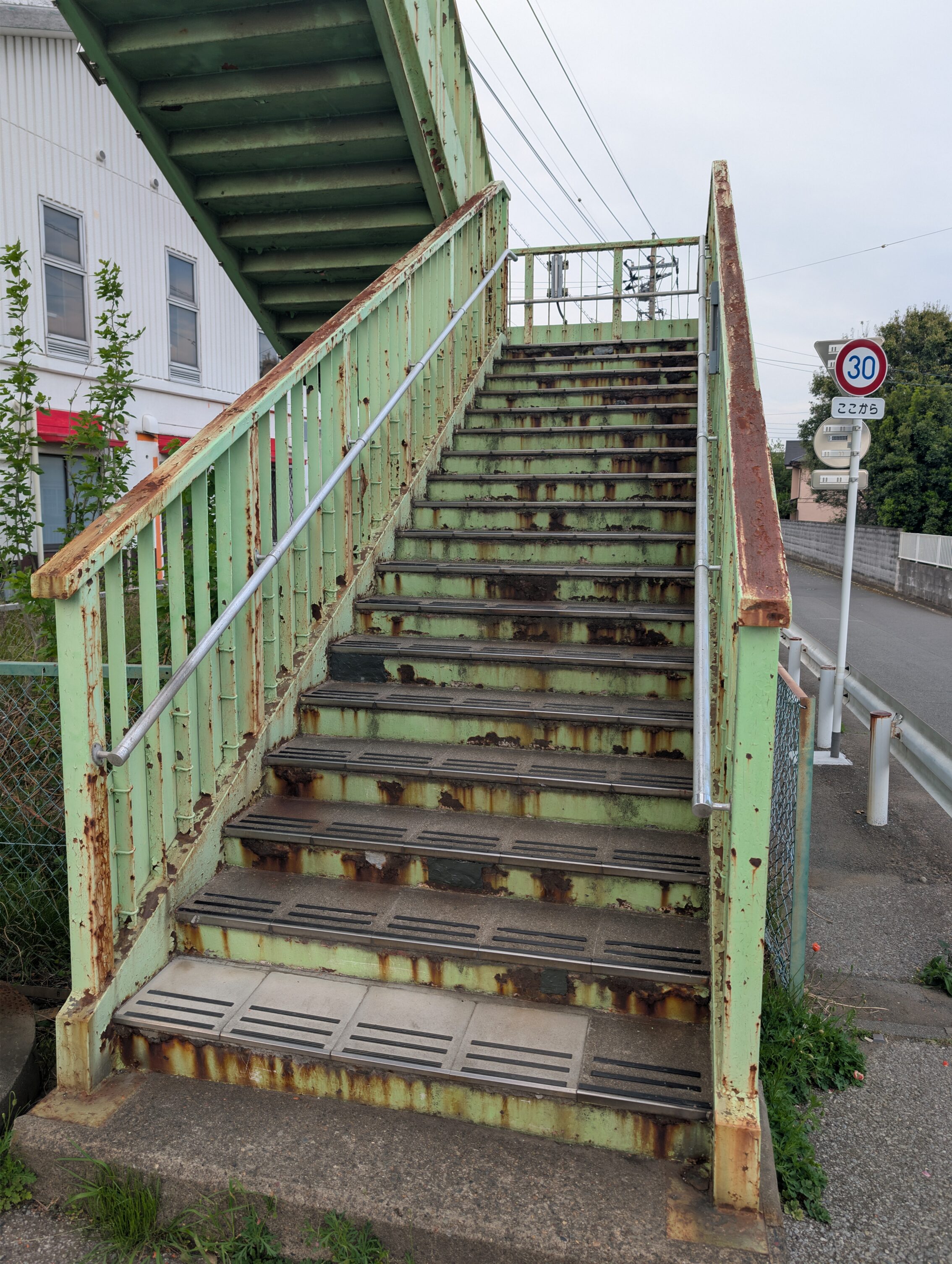 A pedestrian staircase for crossing a street. It is very rusty, and looks quite old and dilapidated.