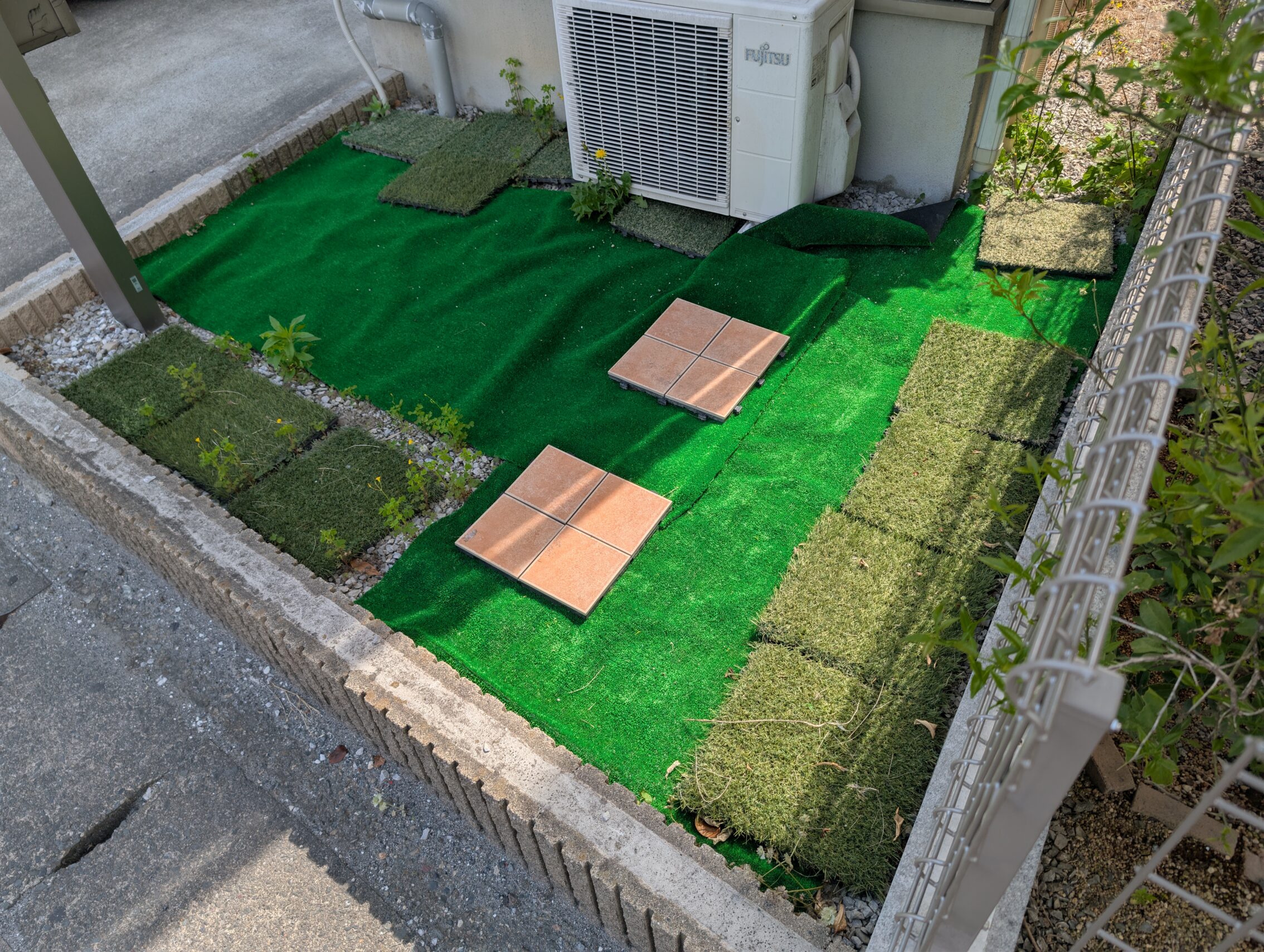 A tiny patch of ground next to a house covered with several types of fake grass.