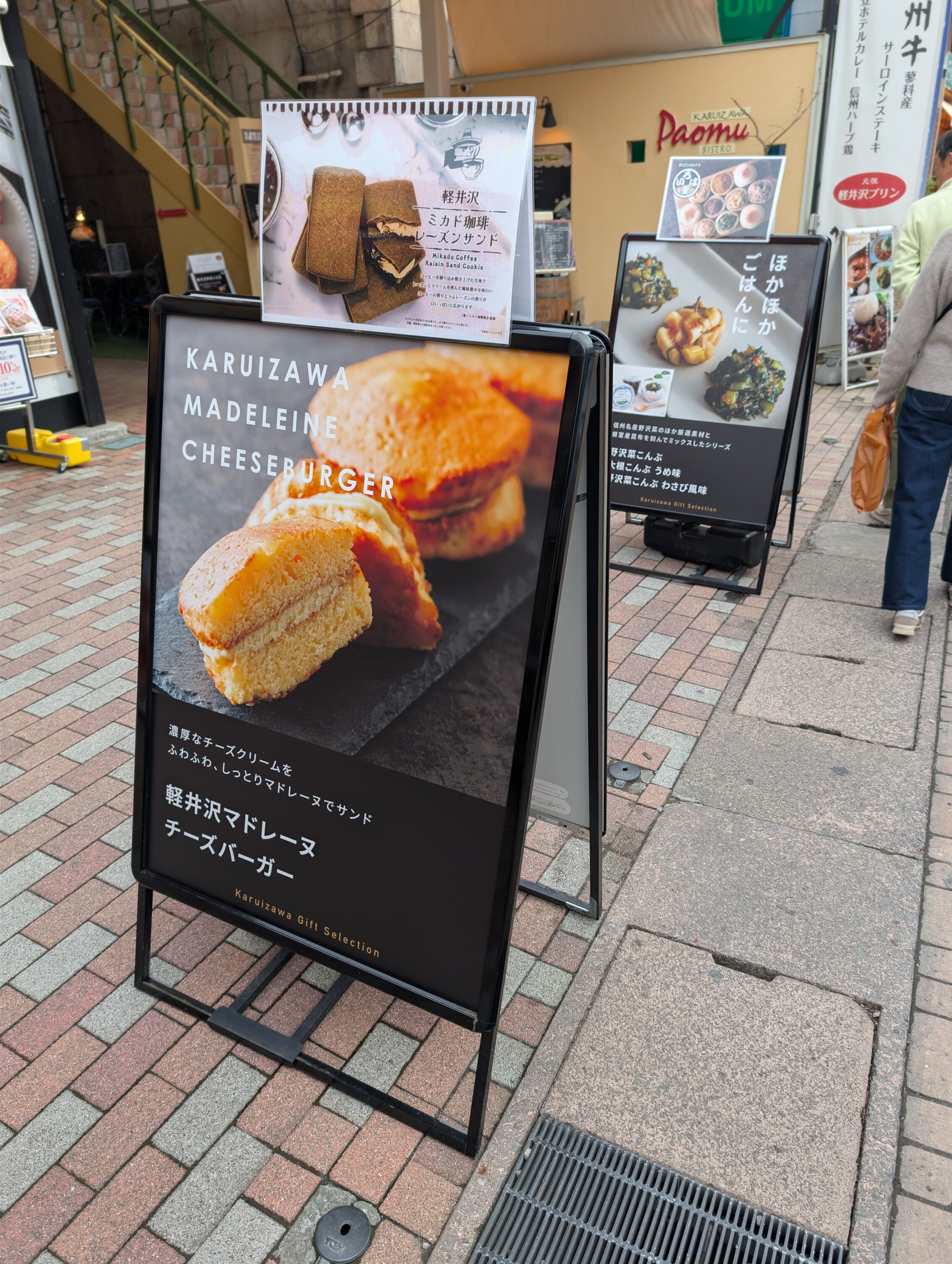 A street ad for a coffee shop that sells madeleine cakes with cheese. The text says "Karuizawa Madeleine Cheeseburger"