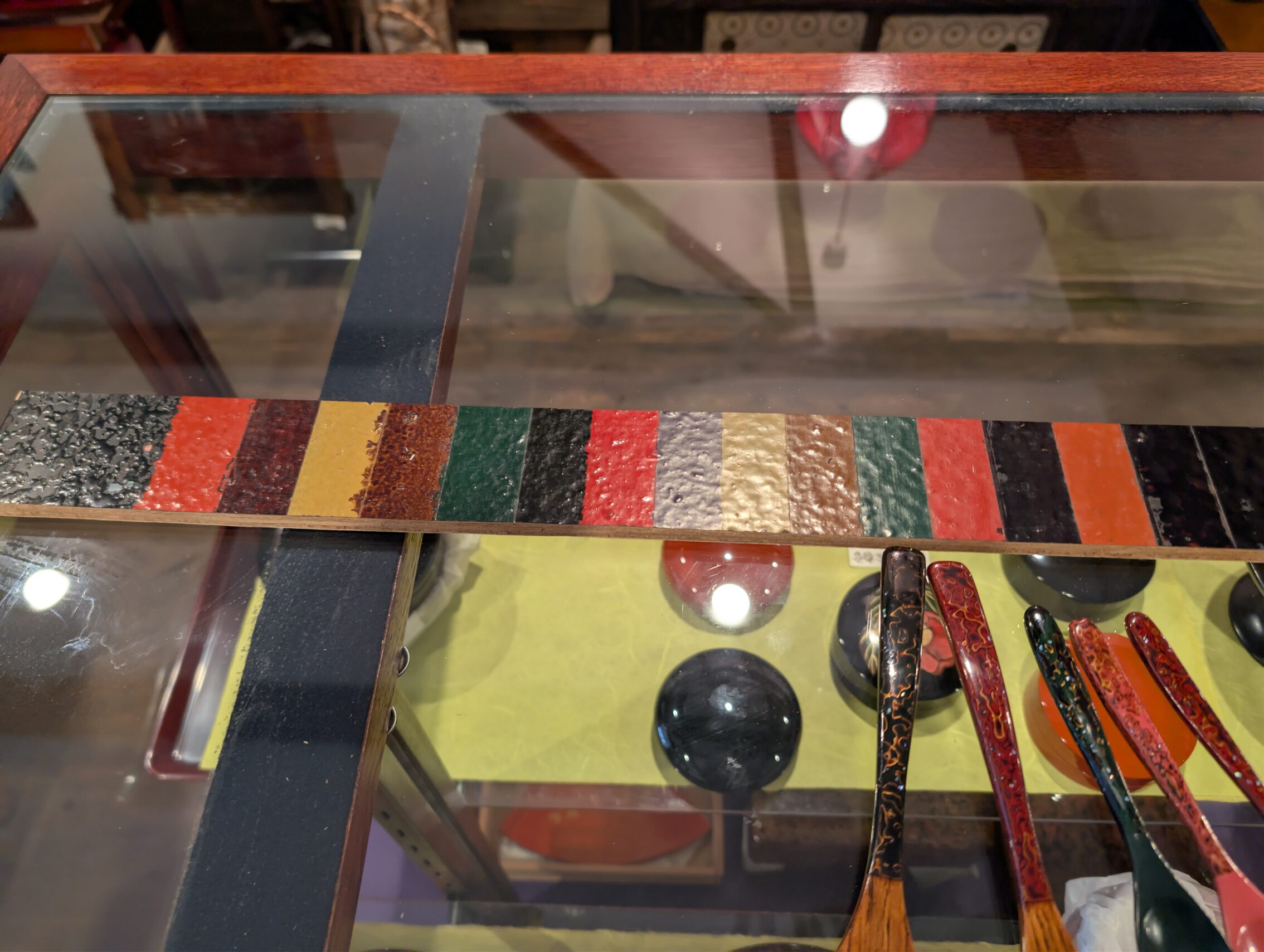 A table with a couple of wooden objects with urushi, as well as a stick showing the various colour variants that the craftsmen use.