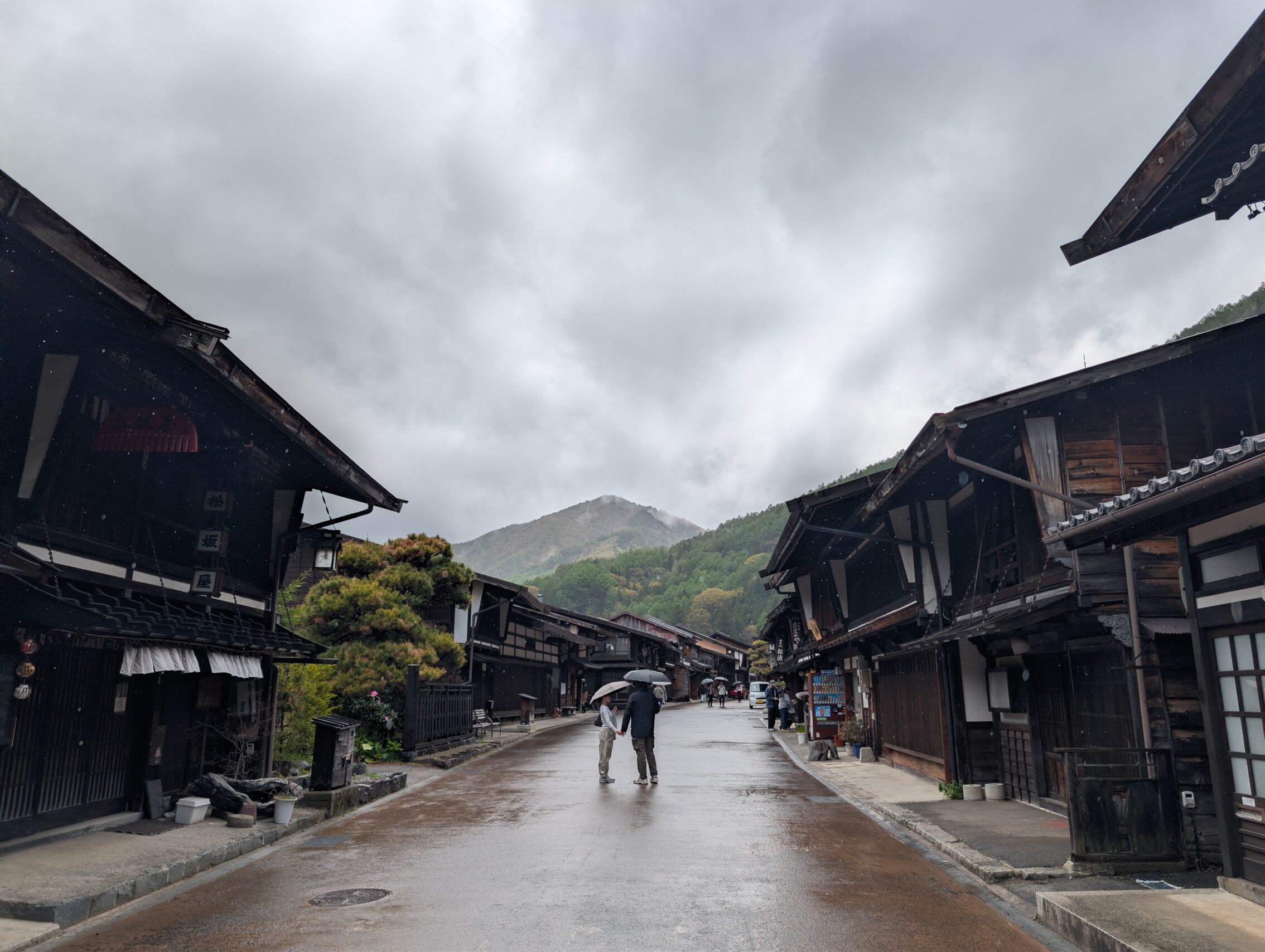 A couple under umbrellas walking along an otherwise deserted street in Narai-juku.