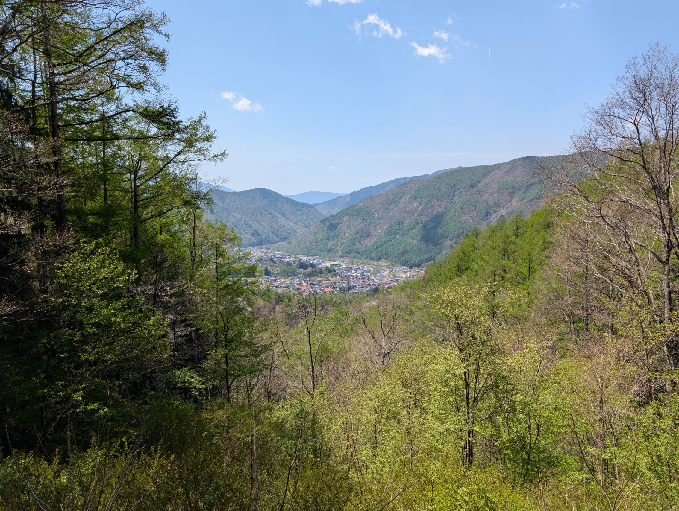 A view of a river valley, with a blue sky and trees. The Kiso river is in the distance.