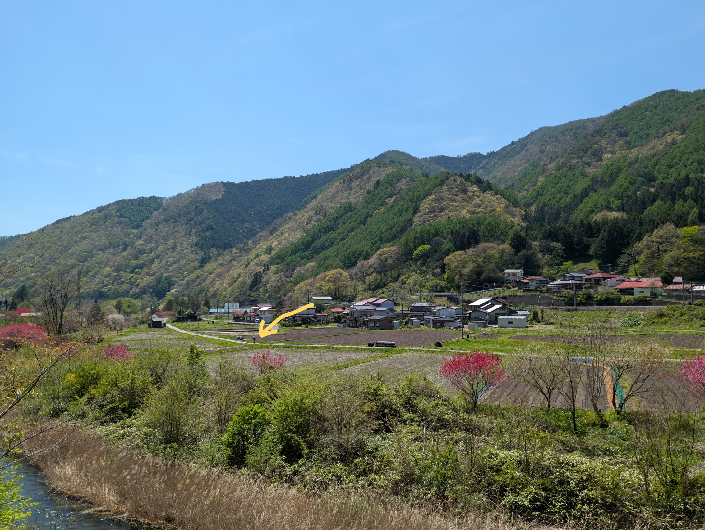 A view across the Kiso river valley, with a small hiker on a road. There is a large painted arrow pointing at the hiker.
