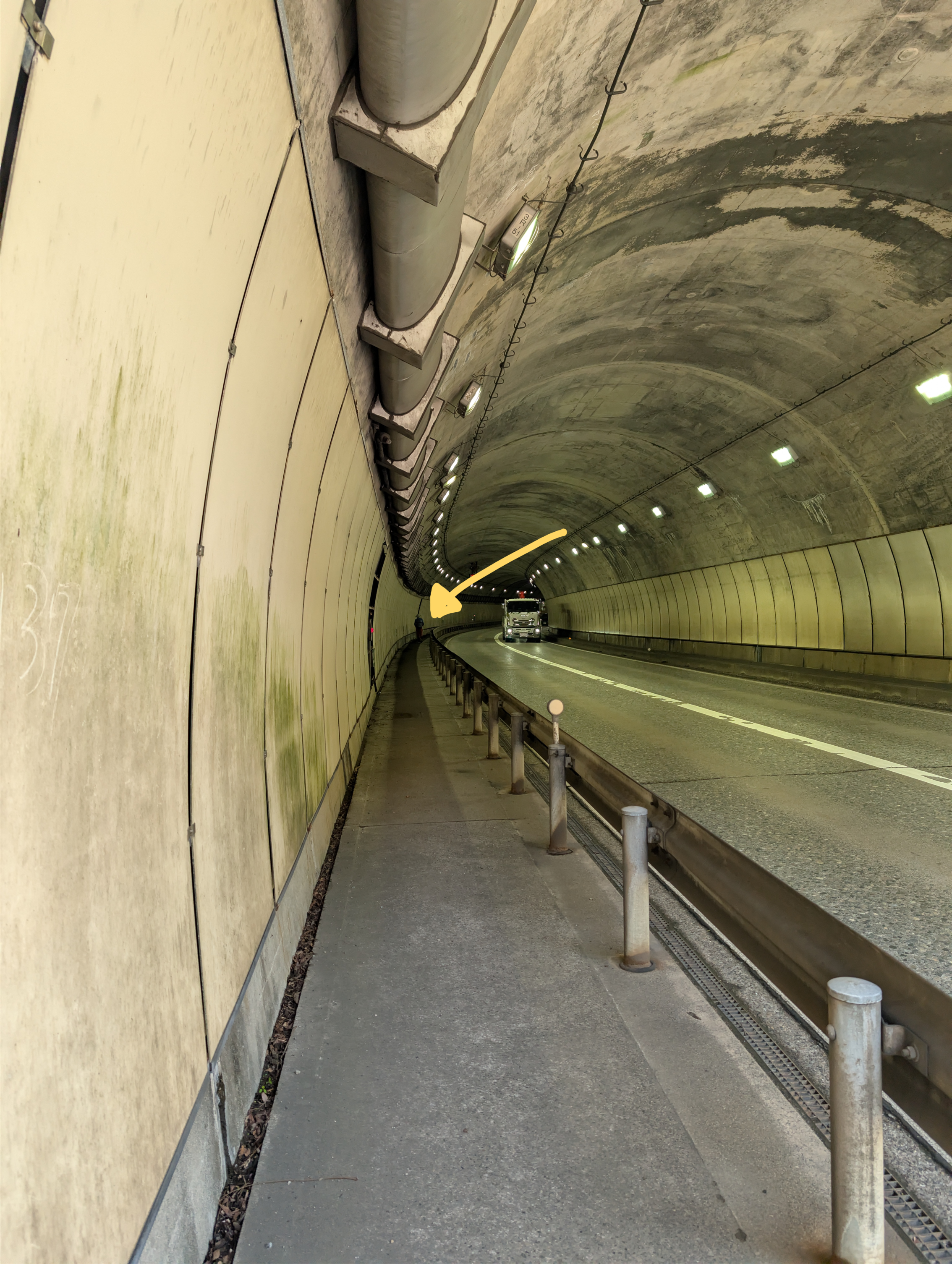 The entrance to a car tunnel, with a hiker further in. A yellow arrow points to the hiker.