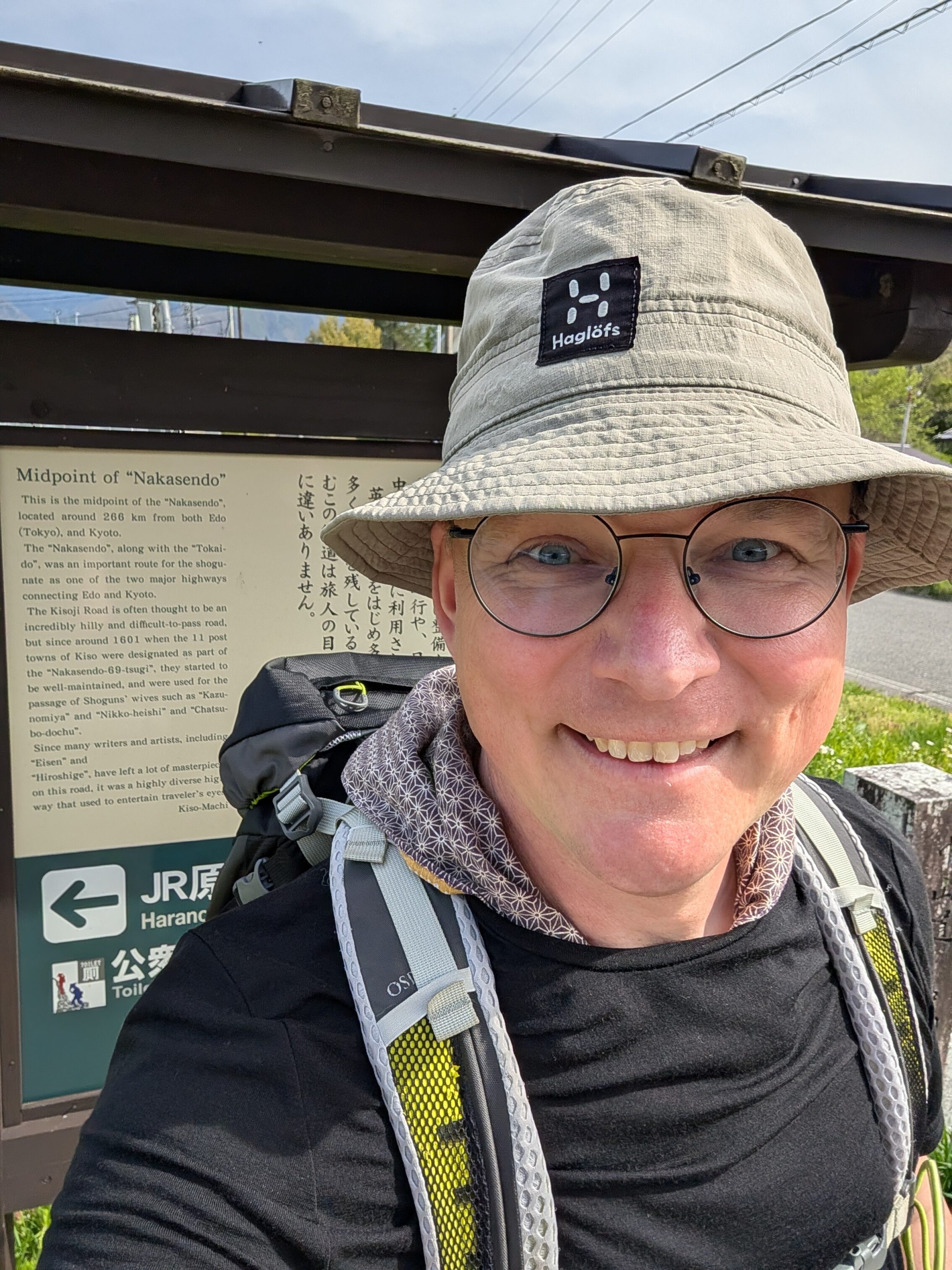 Smiling hiker in front of information board describing the spot to be the half-way point of the Nakasendō.