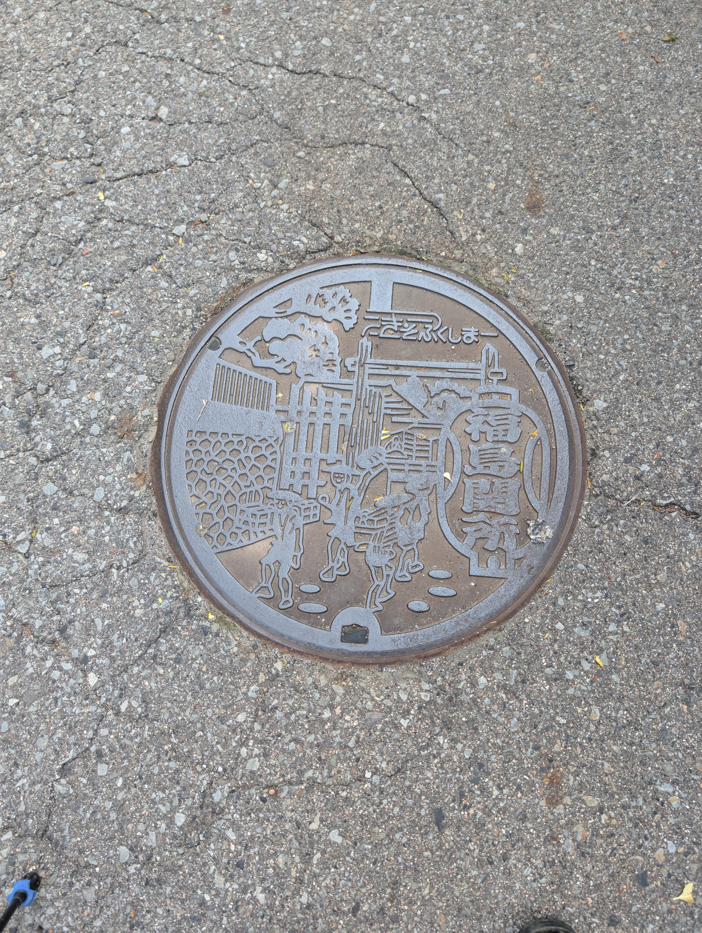 Manhole cover showing Edo period travellers passing the Fukushima-juku barrier gate, the shekisho.