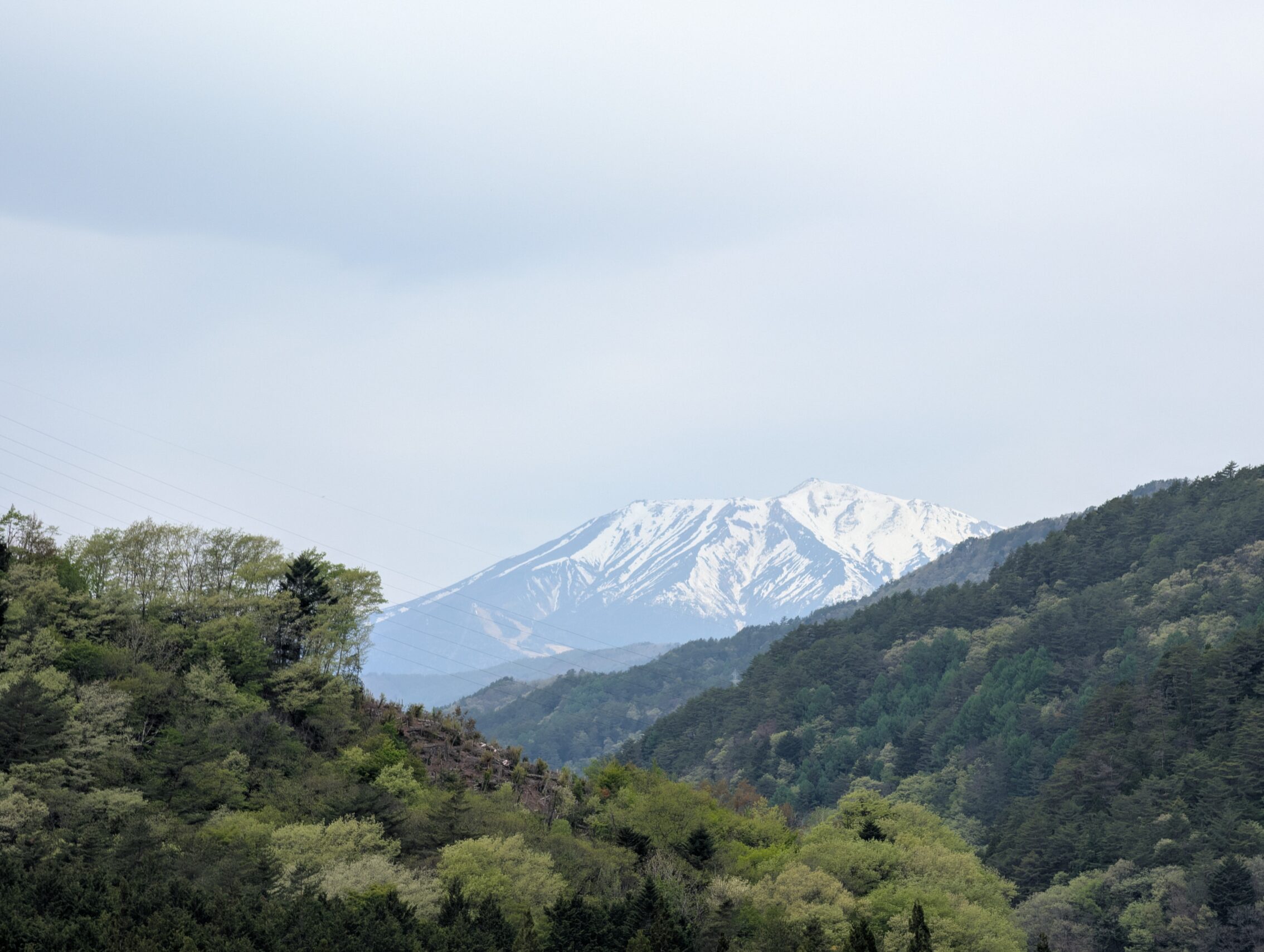 Snowclad Mount Ontaki in the distance, flanked by smaller, mountains with forests.