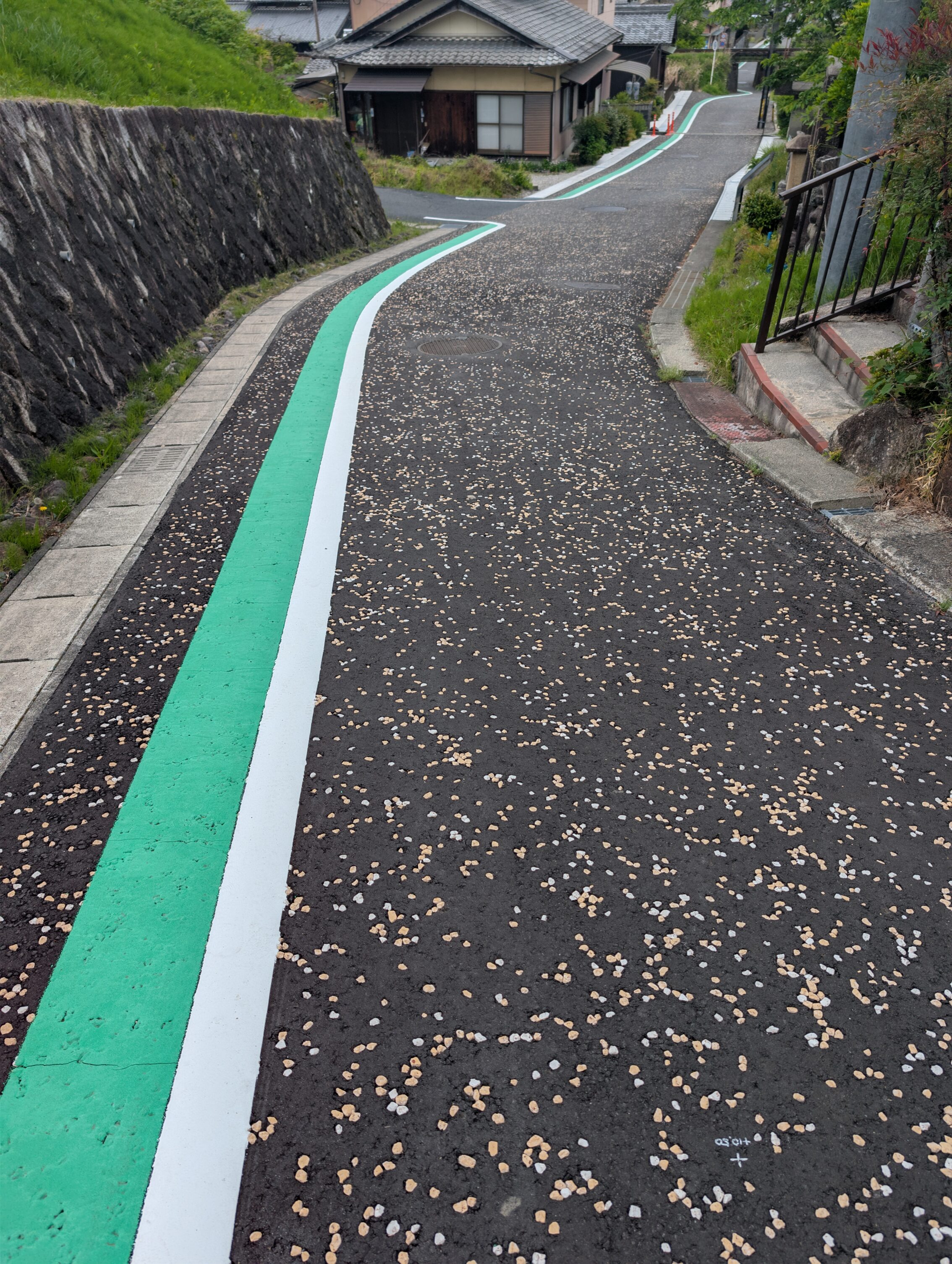 A paved road with a painted green line indicating a pavement. The asphalt is speckled with white and yellow stones.