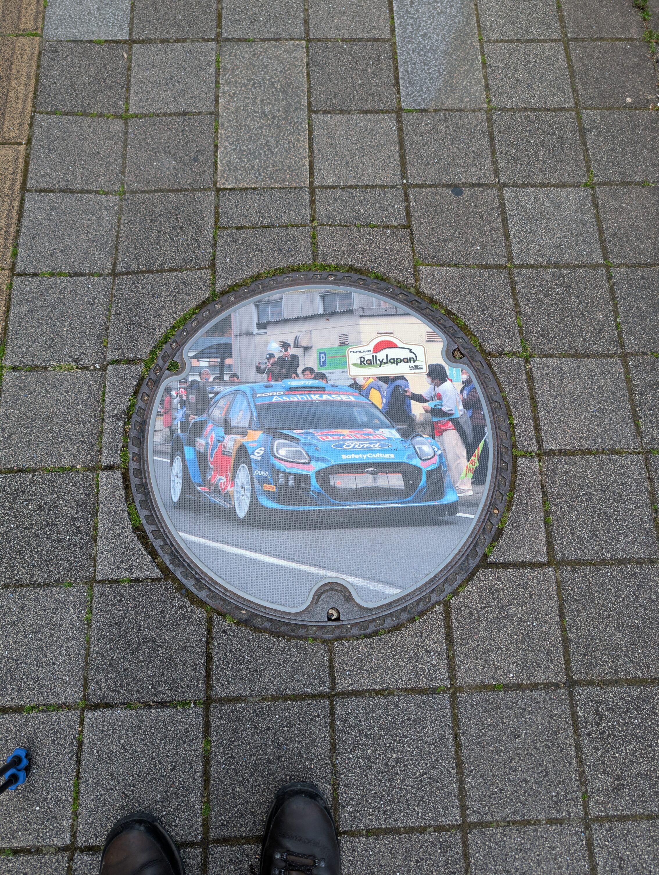 Manhole cover showing a modern rally racing car in full colour.