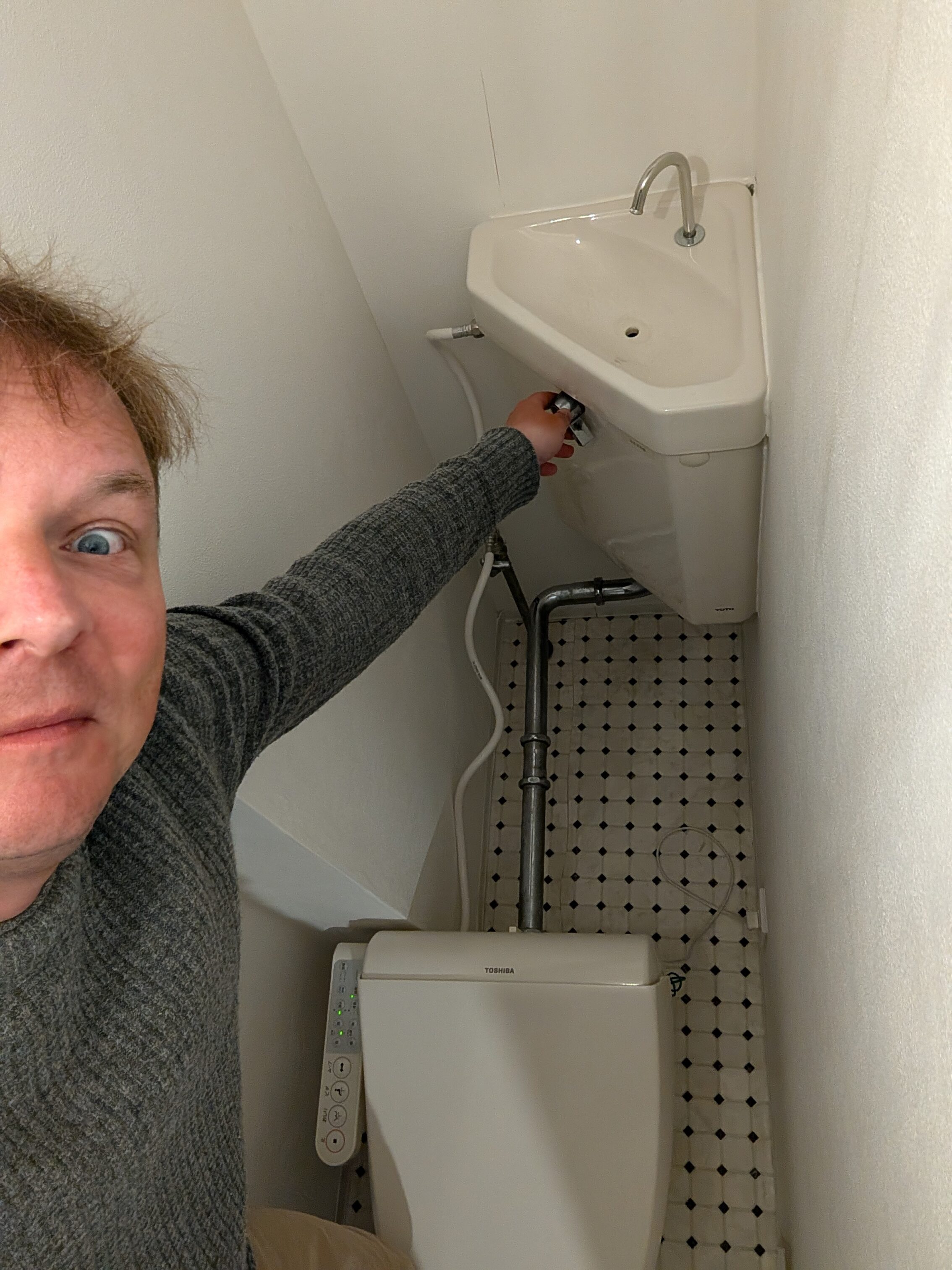 A person trying to flush a toilet, but the lever is placed about a metre behind the toilet, and is very hard to reach.