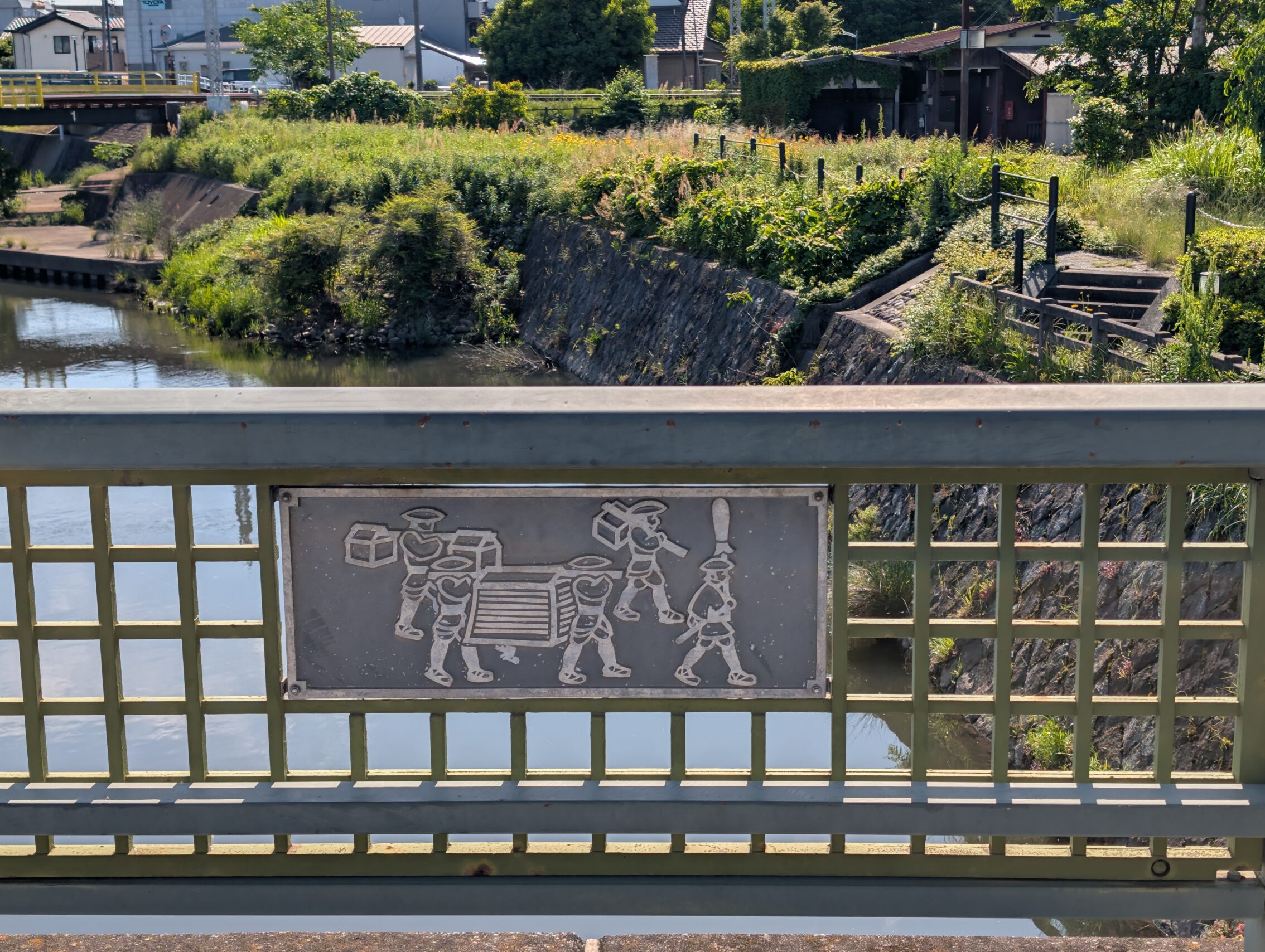 A bridge railing with a plaque showing people carrying goods.