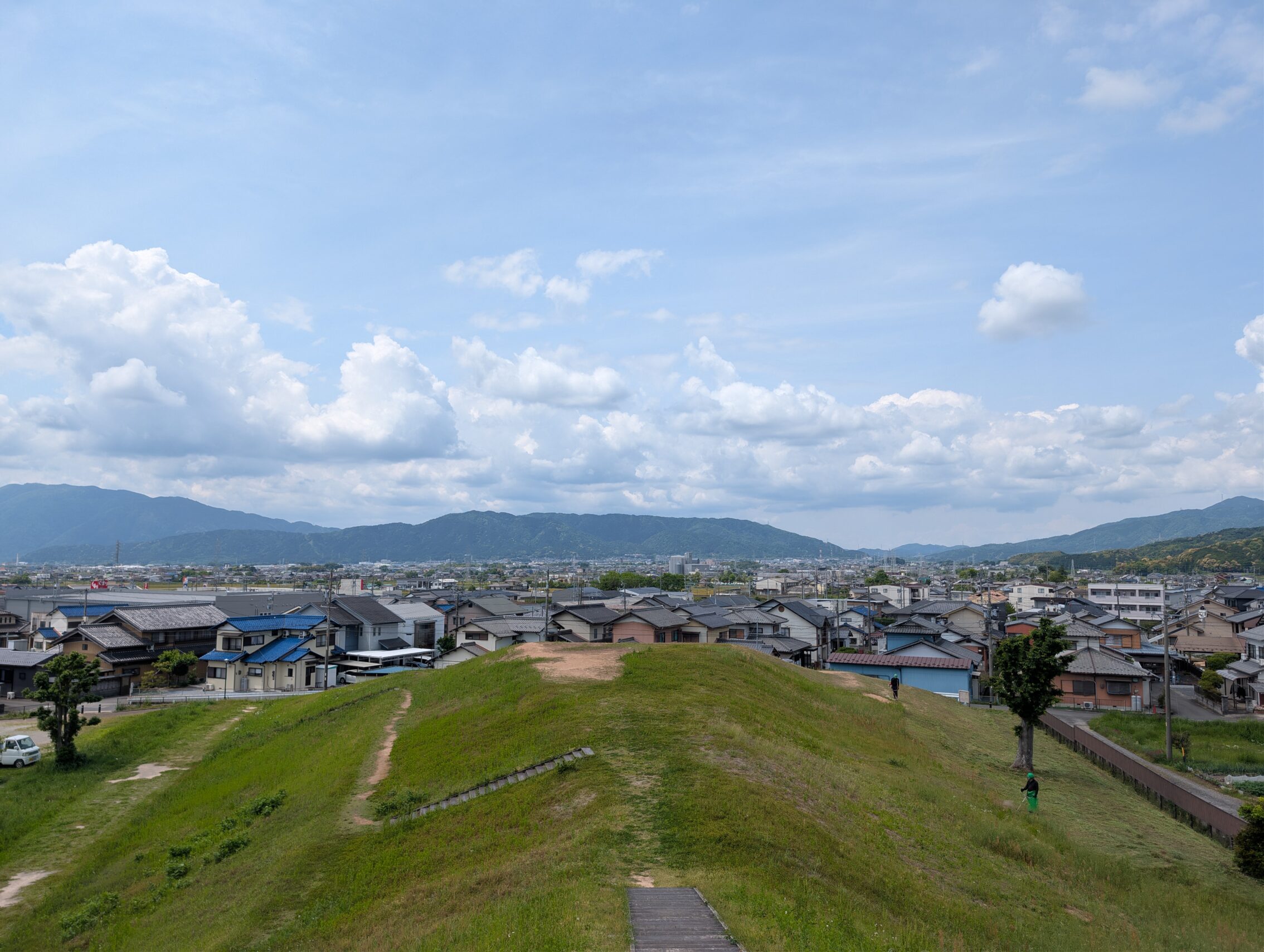 A view of the countryside with mountains in the background. In the near foreground is a geometrical hill formation.