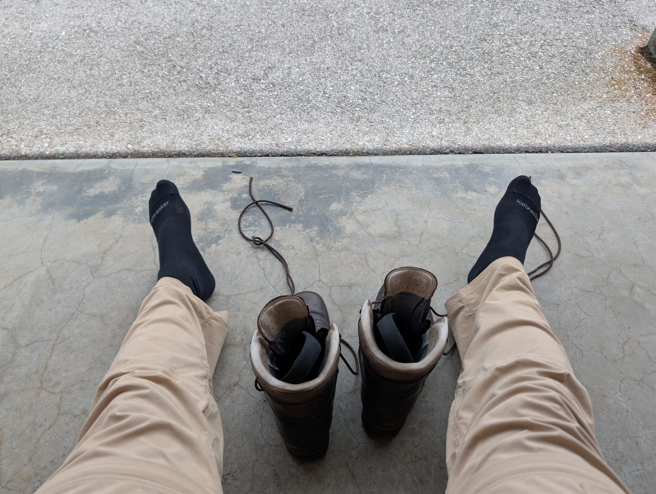 A pair of legs next to a pair of untied boots.
