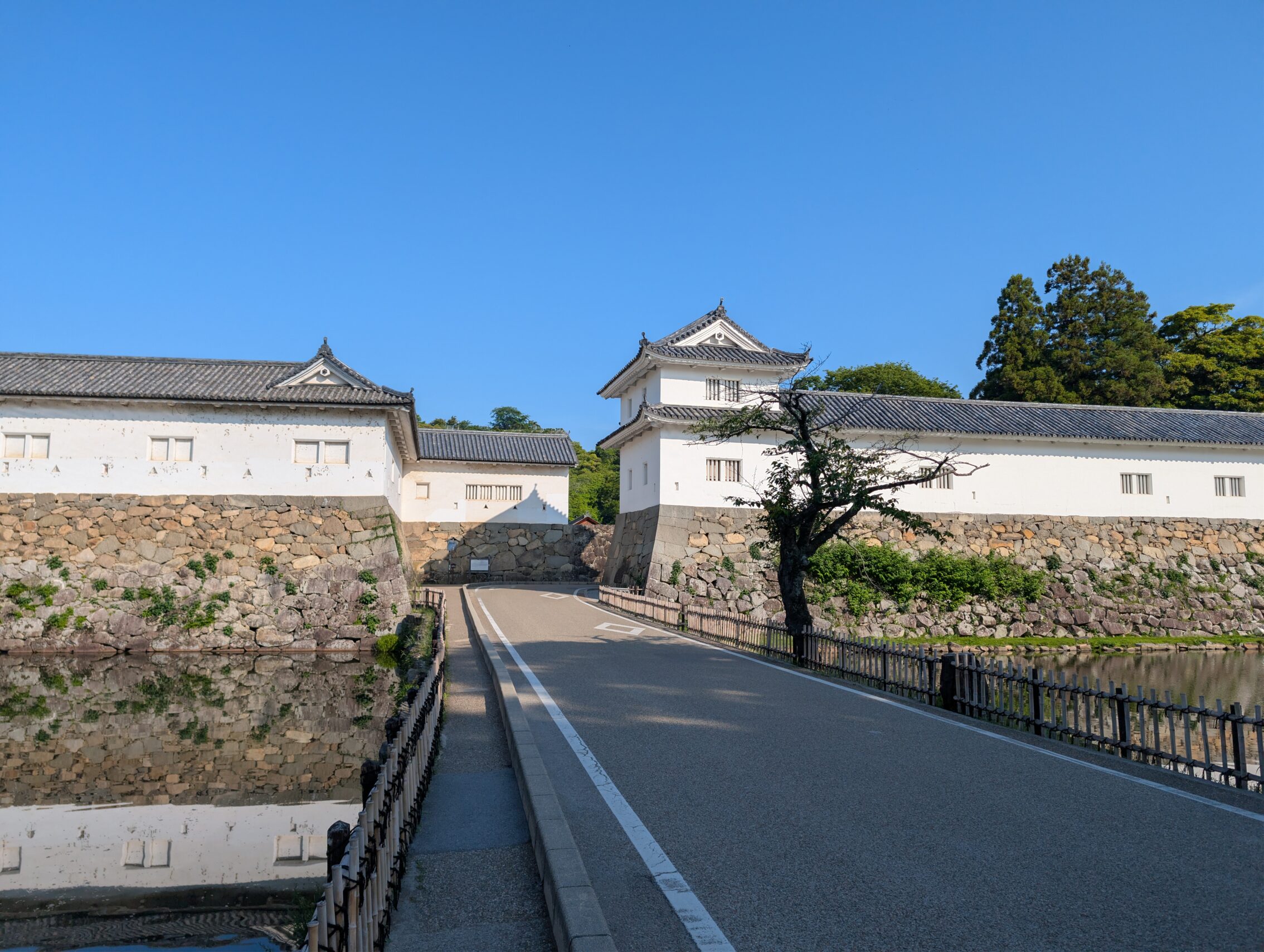 A bridge across a moat, towards white castle walls, and the entrance gate.