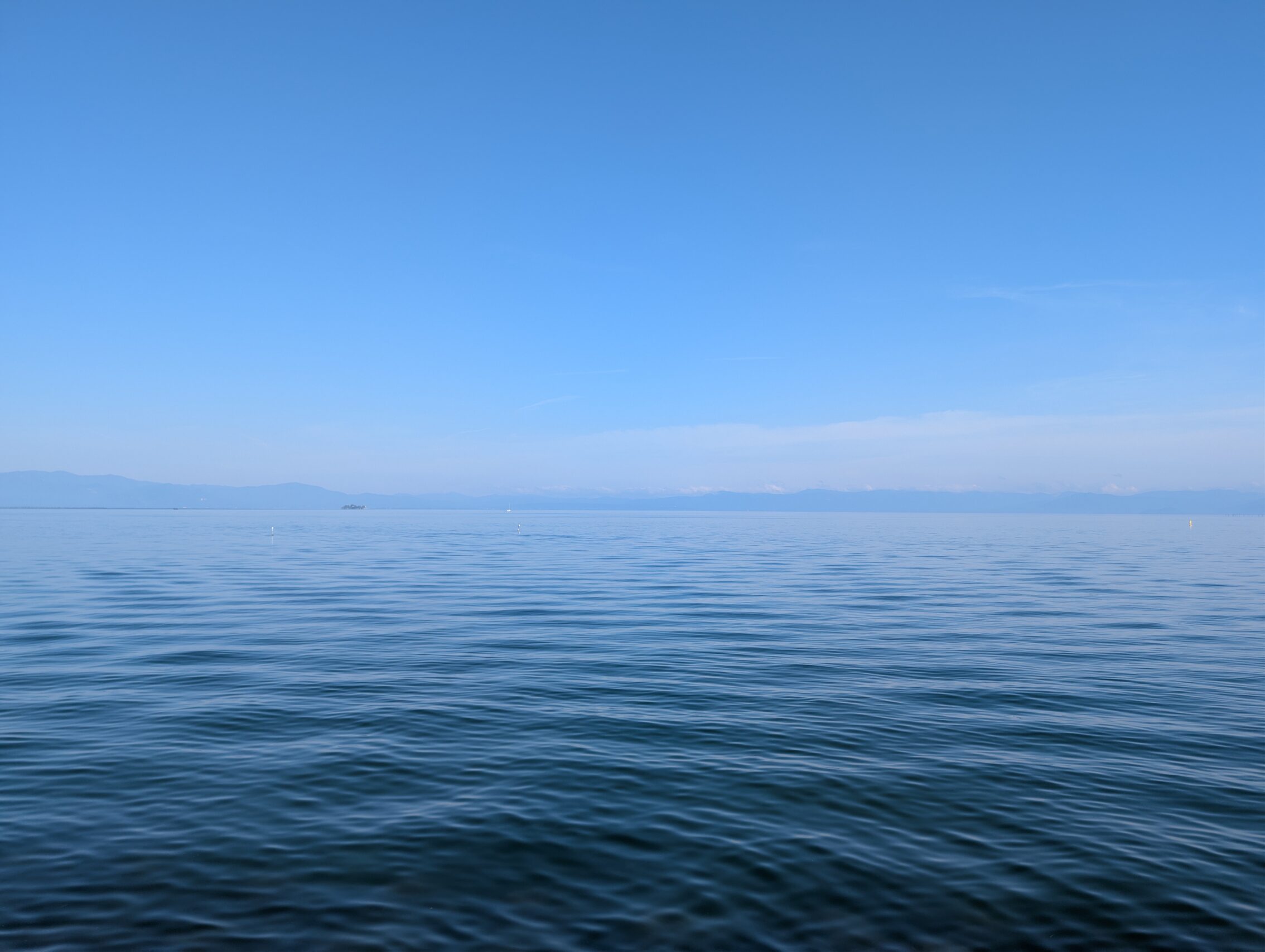 A lake that disappears into the distance, with a blue sky, and hazy clouds on the horizon.
