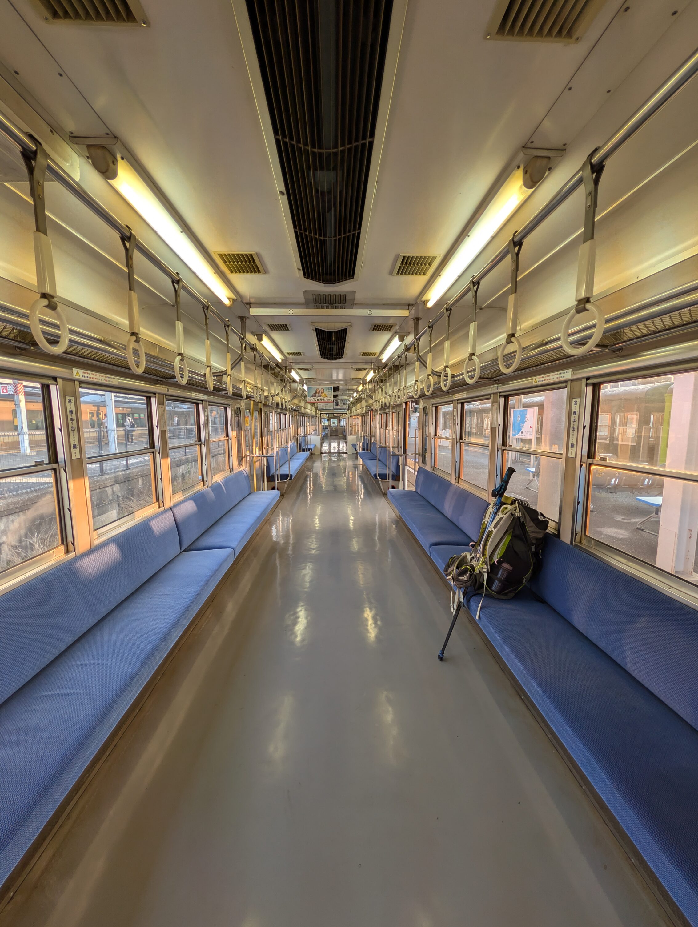 The inside of an empty train, apart from a backpack and a pair of hiking poles.