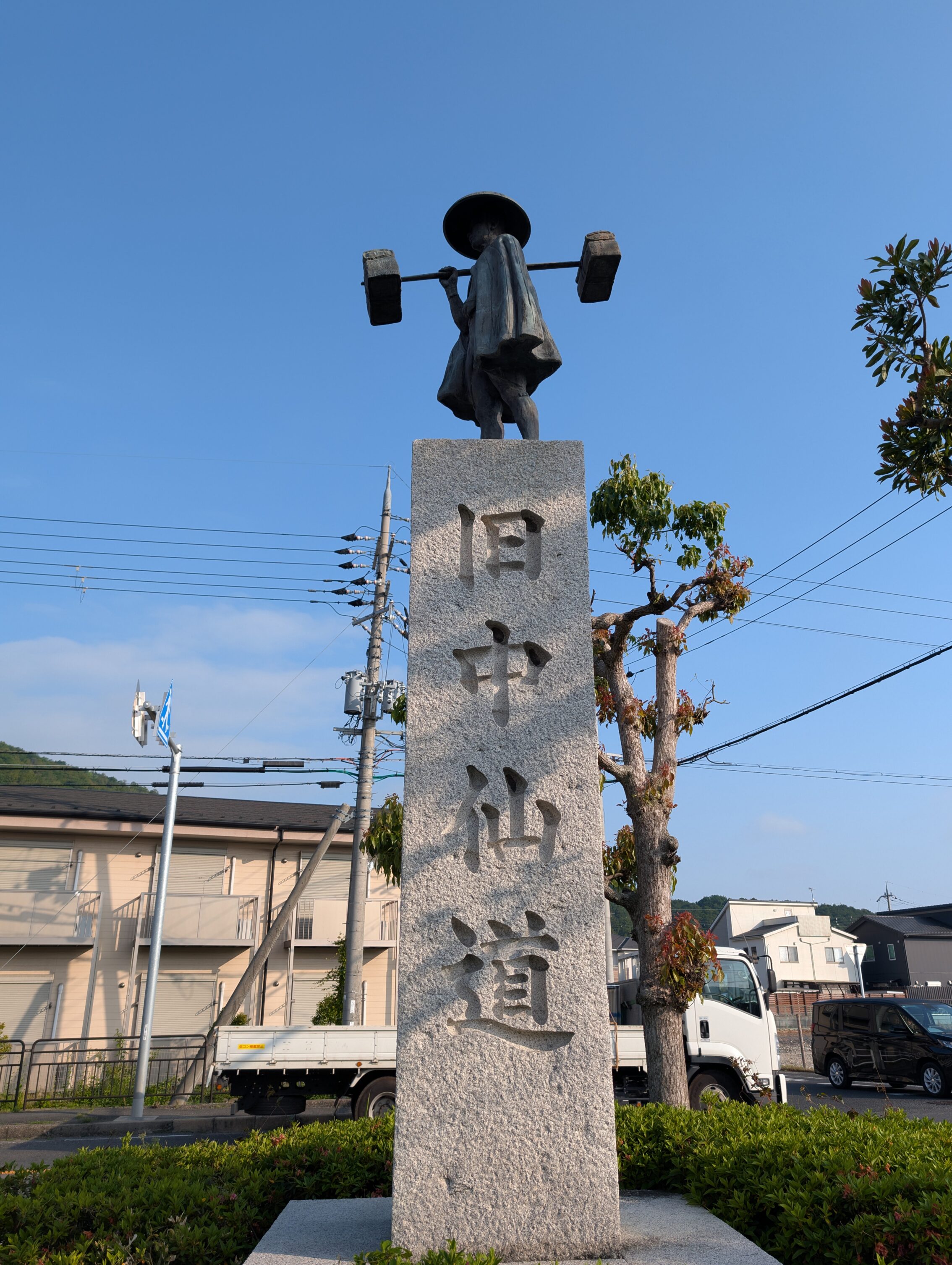 A statue of a man carrying a heavy load, on top of a pedestal with Old Nakasendō carved into it.