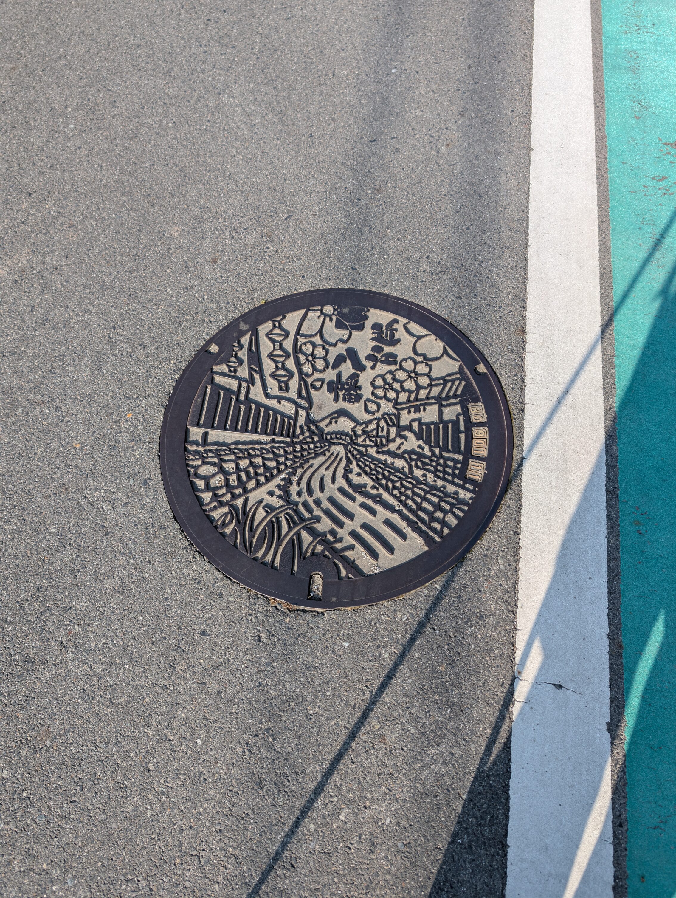Manhole cover showing a river and Edo period houses on both sides.