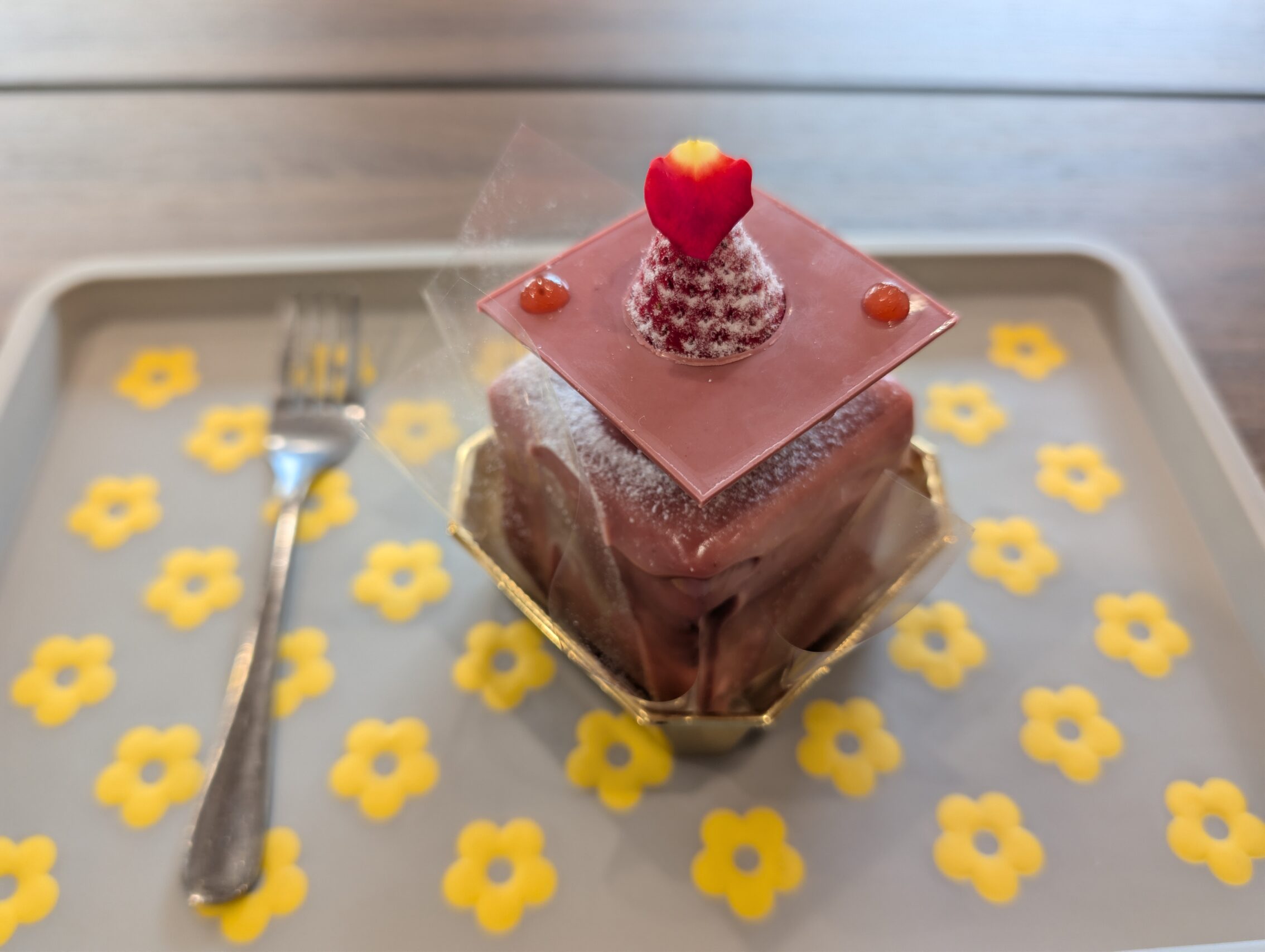 A tray with yellow flowers, a fork, and a chocolate-strwberry cake.